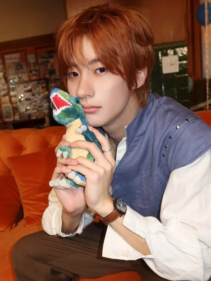 A seated portrait holding a small green dinosaur plush.